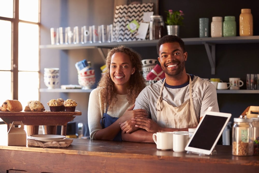 black couple behind counter with muffins and coffee