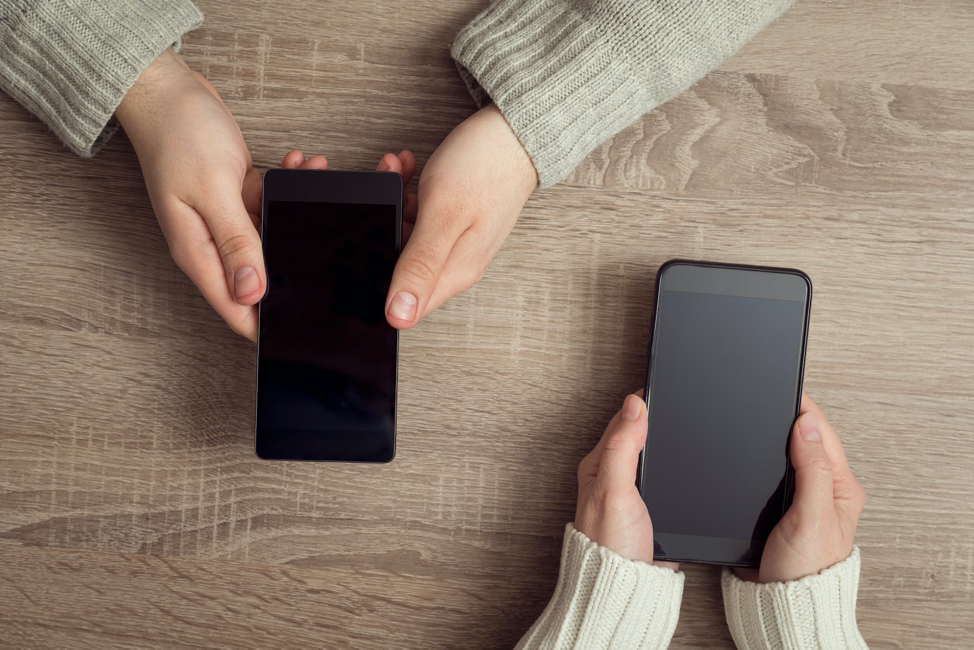 Two women holding phones and leaning on table